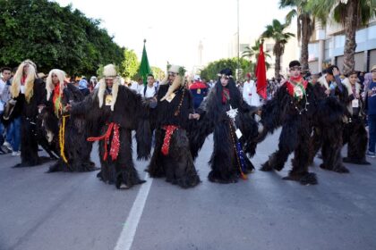 أشخاص يرتدون أزياء تنكرية ملونة في استعراض كرنفالي