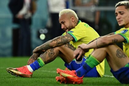رجلان يرتديان قمصان المنتخب البرازيلي يجلسان على أرضية الملعب.
