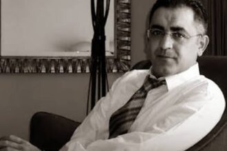 شهاب زريوح يجلس مبتسماً يرتدي نظارة وربطة عنق شبه رسمية