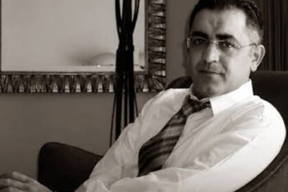 شهاب زريوح يجلس مبتسماً يرتدي نظارة وربطة عنق شبه رسمية
