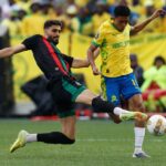 لاعب بالقميص الأصفر والأسود يركل الكرة أمام لاعب بالأسود