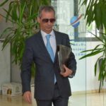 رجل يرتدي بدلة يحمل مجلداً أمام منضدة استقبال.