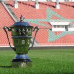 كأس فضية لامعة تقف على عشب أخضر داخل ملعب كرة قدم.
