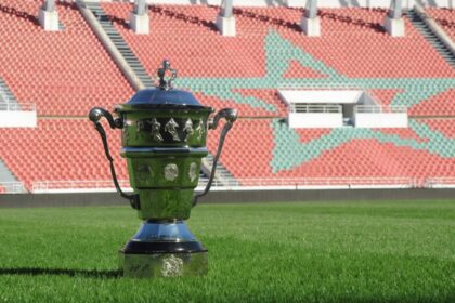 كأس فضية لامعة تقف على عشب أخضر داخل ملعب كرة قدم.