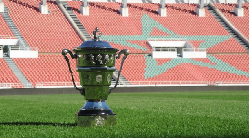 كأس فضية لامعة تقف على عشب أخضر داخل ملعب كرة قدم.