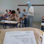 طلاب في قاعة امتحان، أحدهم يمسك ورقة.