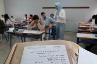 طلاب في قاعة امتحان، أحدهم يمسك ورقة.