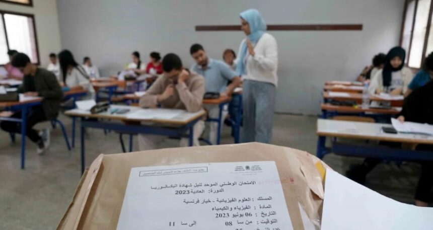 طلاب في قاعة امتحان، أحدهم يمسك ورقة.