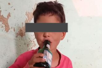 طفل يرتدي قميصًا أحمر ويشرب من زجاجة