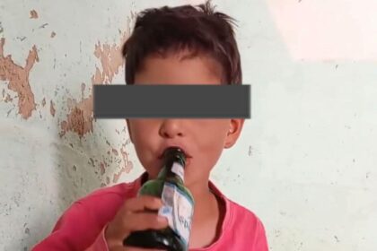 طفل يرتدي قميصًا أحمر ويشرب من زجاجة