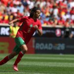 لاعب كرة قدم يرتدي قميصًا أحمر يحمل الرقم 6 يجري بالملعب.