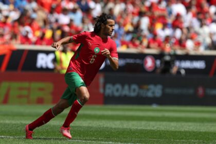 لاعب كرة قدم يرتدي قميصًا أحمر يحمل الرقم 6 يجري بالملعب.
