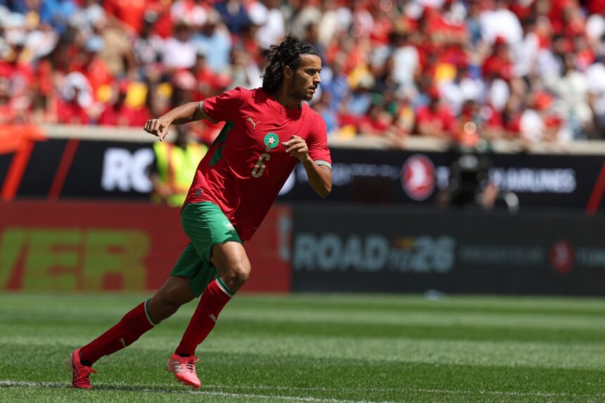 لاعب كرة قدم يرتدي قميصًا أحمر يحمل الرقم 6 يجري بالملعب.