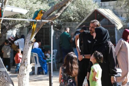 رجل يتحدث مع زبون، وبجواره ببغاء على شجرة.