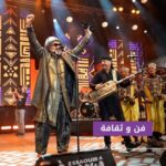 رجل بقبعة يغني أمام الميكروفونات مع فنانين آخرين