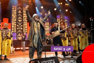 رجل بقبعة يغني أمام الميكروفونات مع فنانين آخرين