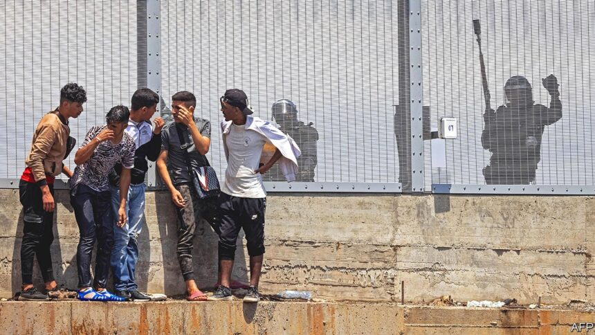 مهاجرون يقفون عند سياج حدودي