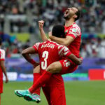 لاعبان من النشامى يحتضنان بعضهما، واللاعب رقم 11 يقف بجانبهما.