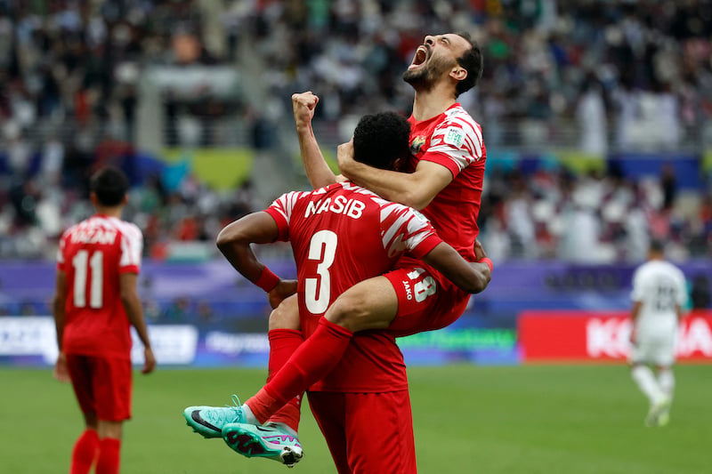 لاعبان من النشامى يحتضنان بعضهما، واللاعب رقم 11 يقف بجانبهما.