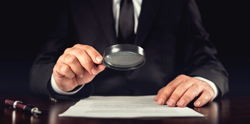 شخص يدقق في وثيقة باستخدام عدسة مكبرة على طاولة.