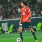 لاعب كرة قدم بقميص أحمر يركض بالكرة في الملعب.