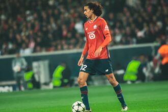 لاعب كرة قدم بقميص أحمر يركض بالكرة في الملعب.