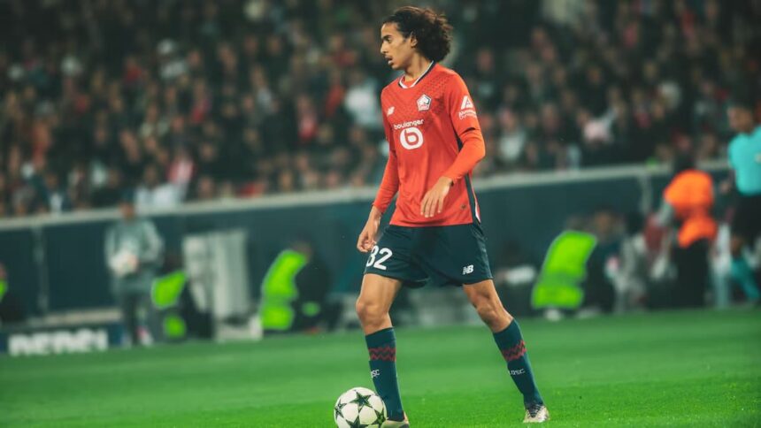 لاعب كرة قدم بقميص أحمر يركض بالكرة في الملعب.