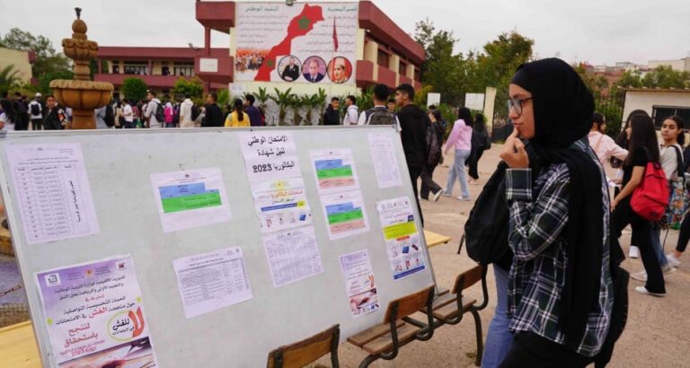 امرأة تقف أمام لوحة نتائج البكالوريا المعلقة.