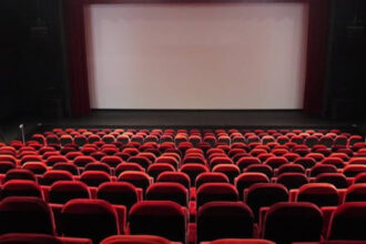 قاعة سينما فارغة بمقاعد حمراء وشاشة عرض بيضاء.