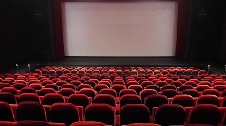 قاعة سينما فارغة بمقاعد حمراء وشاشة عرض بيضاء.