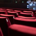 مقاعد حمراء فارغة في قاعة سينما، أضواء خافتة.