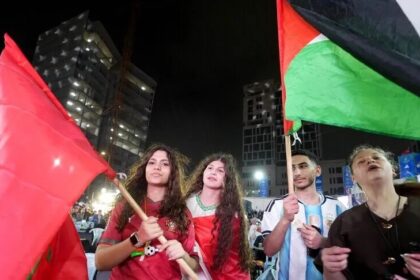 أشخاص يرتدون اللون الأحمر ويرفعون الأعلام في مدرجات كرة القدم.