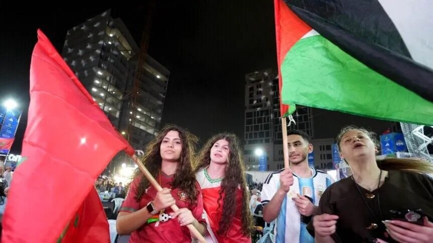 أشخاص يرتدون اللون الأحمر ويرفعون الأعلام في مدرجات كرة القدم.