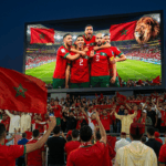 مشجعون يلوحون بالأعلام أمام شاشة عرض كبيرة في الملعب