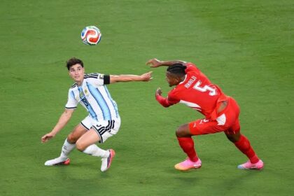لاعب كرة قدم يرتدي قميصًا أحمر وأبيض في ملعب عشبي