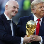 رجلان يبتسمان ويحملان كأس كرة قدم كبير.