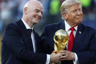 رجلان يبتسمان ويحملان كأس كرة قدم كبير.