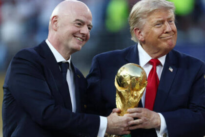 رجلان يبتسمان ويحملان كأس كرة قدم كبير.