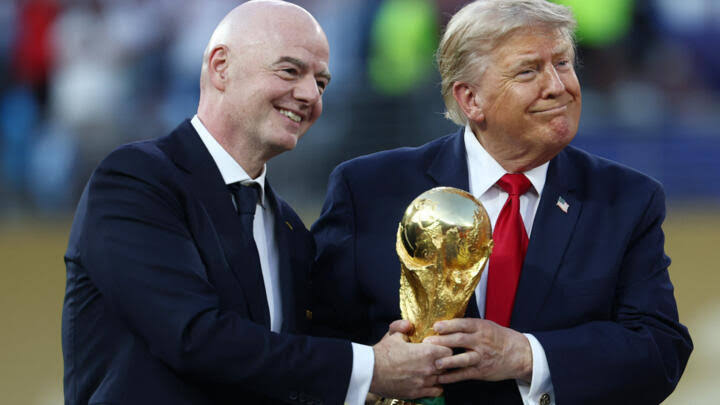 رجلان يبتسمان ويحملان كأس كرة قدم كبير.
