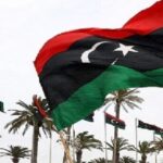 علم ليبي يرفرف في السماء، ألوانه حمراء وسوداء وخضراء.