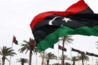 علم ليبي يرفرف في السماء، ألوانه حمراء وسوداء وخضراء.
