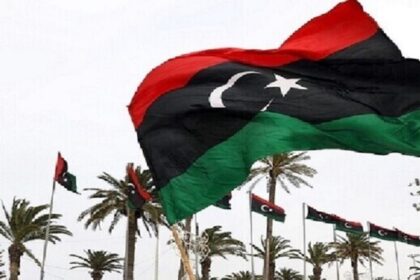 علم ليبي يرفرف في السماء، ألوانه حمراء وسوداء وخضراء.