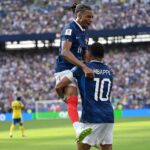 لاعب كرة قدم فرنسي يرتدي قميص مبابي يحتفل مع زميله.
