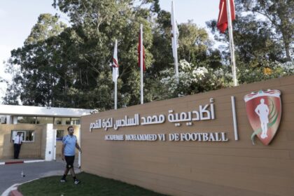 رجل يقف أمام لافتة أكاديمية محمد السادس لكرة القدم