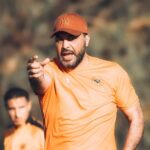 معين الشعباني يشير بيده في الزي البرتقالي