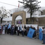 مجموعة من المتظاهرين أمام مبنى أبيض مفتوح في يوم غائم.
