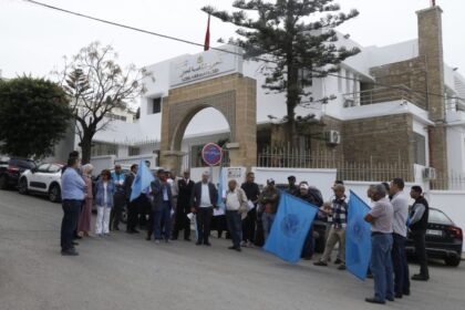 مجموعة من المتظاهرين أمام مبنى أبيض مفتوح في يوم غائم.
