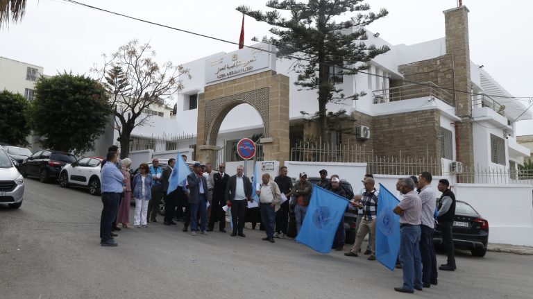 مجموعة من المتظاهرين أمام مبنى أبيض مفتوح في يوم غائم.