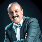 سعيد الناصري مبتسماً يرتدي نظارة وبدلة سوداء وربطة عنق
