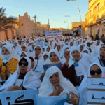 امرأة ترفع لافتة وسط حشد كبير في منطقة صحراوية.